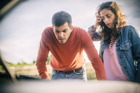 A young couple had a car breakdown on the road. They stand very upset, open the hood and try to fix the broken engineの写真素材