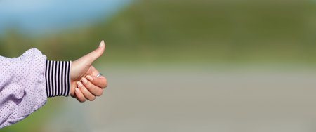 Close-up detail view of female hitchhiker hand with up finger, hitchhiking on a sunny day. Autostop...