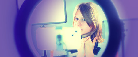 A young female online Influencer makes video content about teenage life. She uses a smartphone and a studio light to recordの写真素材