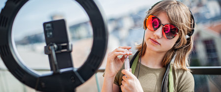 Influencer young woman recording video on smartphone and lighting herself with ring lamp. Broadcast communicates with followers in social networks.の写真素材