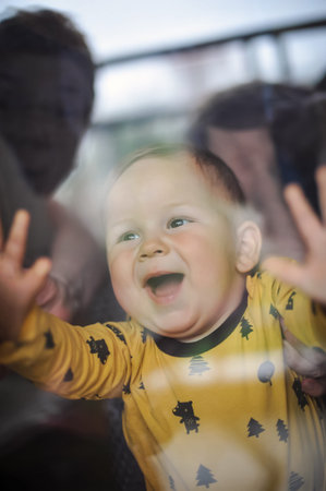 Portrait of cute smiling baby boy looks through the window. Joy and happiness concept. Love and family emotionの写真素材