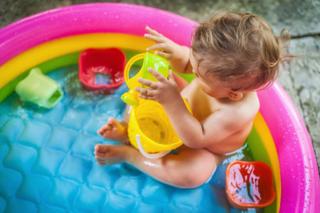Baby boy sitting in a pool at the garden and playing with water toys. Hot summer day in natureの写真素材