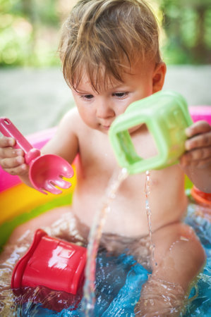 Baby boy sitting in a pool at the garden and playing with water toys. Hot summer day in natureの写真素材