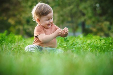 Cute laughing baby having fun sitting on grass in sunshine day. Summer time, happy babyの写真素材