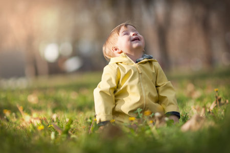 Happy cute and laughing baby boy having fun sitting on grass in sunshine day. Joy and happiness...