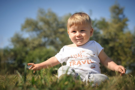 Cute laughing baby having fun sitting on grass in sunshine day. Summer time, happy babyの写真素材