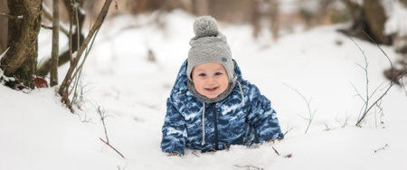 Adorable laughing toddler boy playing outside in snow on beauty winter day. Child exploring nature. Winter activities for small kidsの写真素材
