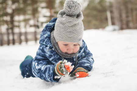Adorable laughing toddler boy playing outside in snow on beauty winter day. Child exploring nature. Winter activities for small kidsの写真素材