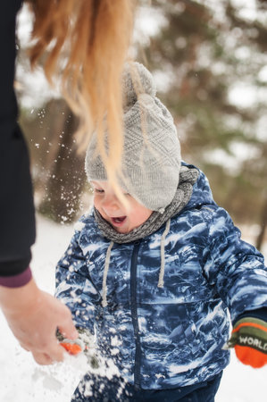 Adorable laughing toddler boy playing outside in snow on beauty winter day. Child exploring nature. Winter activities for small kidsの写真素材