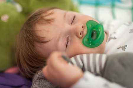 Cute baby boy sleeps peacefully with a pacifier, holding his favorite stuffed toy, under soft daylight. Embodiment tranquility and innocenceの写真素材