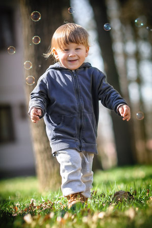 Happy smiling cute toddler delights in chasing floating soap bubbles, bathed in sunlight amidst nature. Love and family conceptの写真素材