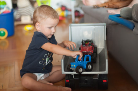 A young child sits on the floor of a comfortable living room, focused on arranging colorful toy trucks. Bright toys and a playful atmosphere fill the space, evoking a sense of joy.の写真素材
