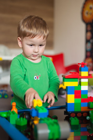 A young child in a green shirt concentrates on building with colorful blocks in a playful indoor space. Bright toys surround him as he showcases his creativity.の写真素材