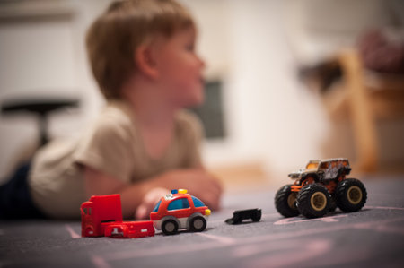 A young child enjoys playtime on the floor surrounded by colorful toy cars and a monster truck, creating a lively atmosphere in a warm indoor setting.の写真素材