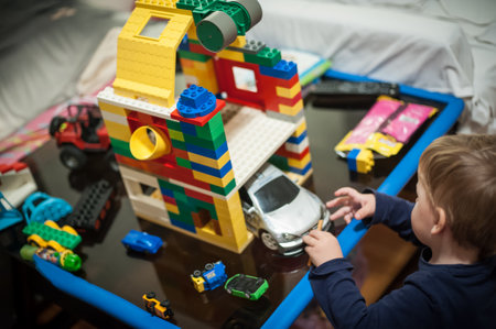 A young child engages in creative play, building a garage structure using colorful building blocks. Various toy cars surround them, emphasizing a fun and imaginative environment.の写真素材