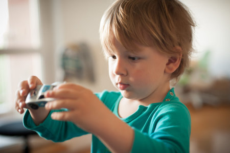 A little child, focused and curious, explores a toy car while sitting indoors. The warm light...