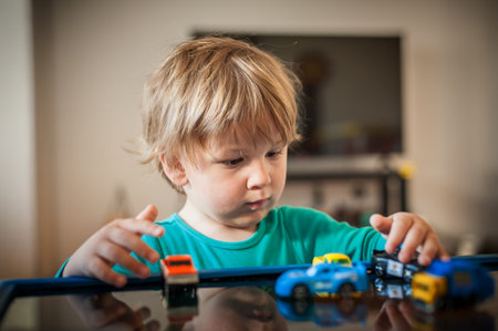 A young boy focuses intently while arranging colorful toy cars on a table. The bright indoor setting creates a playful atmosphere filled with creativity and imagination.の写真素材