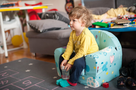 Young child with long hair sits on a soft chair, focused on an activity. The room is filled with toys and bright decor, creating a lively atmosphere in the late afternoon.の写真素材