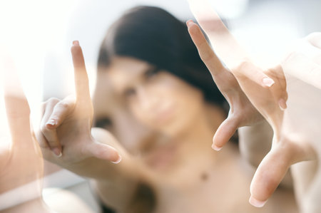 A stylish young girl poses playfully with her hands forming a frame while enjoying a sunny day outdoors. Her trendy outfit reflects the latest fashion and her vibrant personality.の写真素材