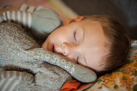 A young child lies asleep on a colorful blanket, holding a soft stuffed toy. The cozy atmosphere and...