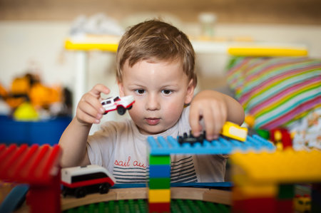 A child concentrates while playing with toy cars and colorful blocks in a cozy indoor environment....