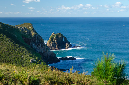In the photograph you can see a rock in the middle of the Atlantic Ocean with a hole caused by the erosion of the sea, the predominant colors are blue and turquoise green, the greens of the vegetation and the browns of autumn.の写真素材
