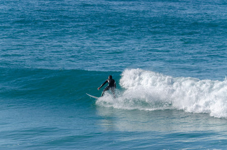 In the photo is a man surfing on a wave with the blue sea in the background