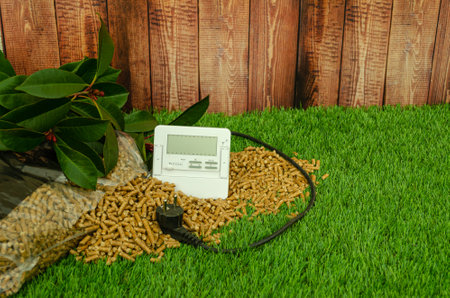 In the photograph you can see a sack of pellets spilled on a grass floor, and a background of a wooden fence, there is a thermostat and a plug.の写真素材