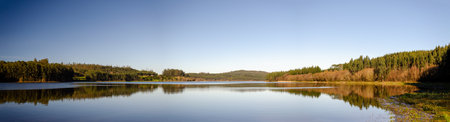 Panoramic view of a lake where the trees are reflected in completely flat water like a mirror.の写真素材