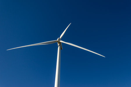 Large white wind turbine producing electricity in a blue sky.の写真素材
