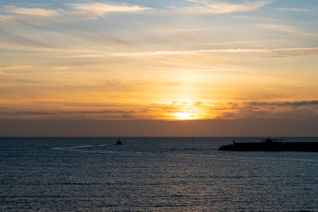 In the photograph you can see a sunset in the blue hour with a tugboat leaving the port.の写真素材