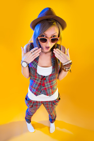 Surprised young girl in glasses and hat looking at viewer. Full height on a yellow background.の写真素材