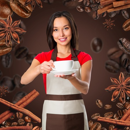 Coffee serving waitress. Young asian barista woman smiling showing cup of coffee. Isolated on brown background. Focus on waitress.の写真素材