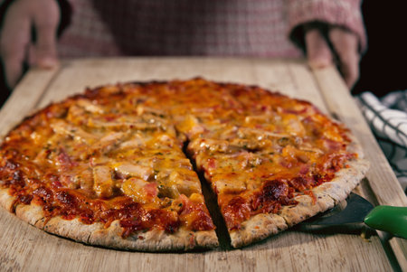 Pizza prepared with pieces of chicken and bacon, presented on a wooden board.の写真素材