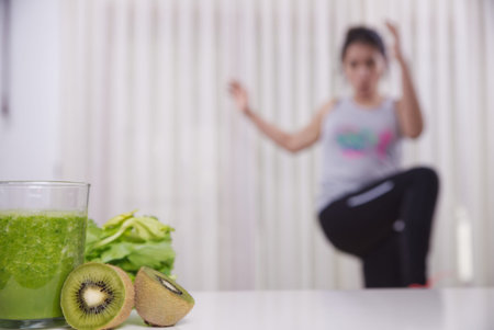 Green smoothie with focused kiwis and woman exercising on unfocused background