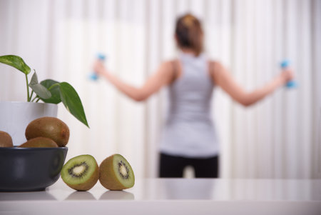 Fruits named kiwis in focus and woman exercising in unfocused background