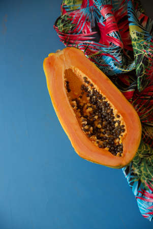 Fresh papaya cut in half on a cheery colored tablecloth, on a blue background.の写真素材