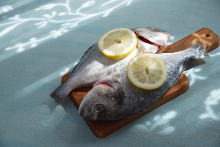 Fish with lemon slices on a wooden board and a light blue table in the background.の写真素材