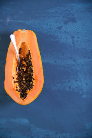 Fresh papaya halved on top of a blue background, on the left side.の写真素材