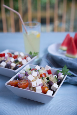 Greek salad in square plates, lemonade and pieces of watermelon on a light blue background.の写真素材