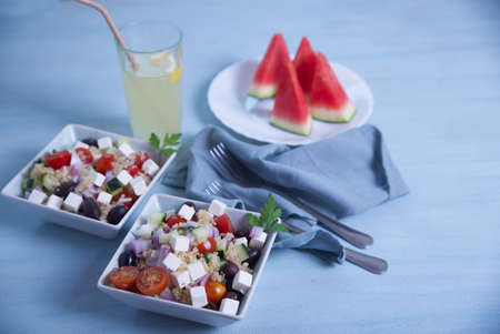 Greek salad in square plates, lemonade and pieces of watermelon on a light blue background.の写真素材