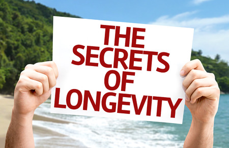 Hands holding cardboard with text Secrets of Longevity on beach backgroundの写真素材