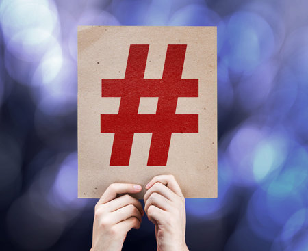 Hands holding cardboard with hashtag symbol on bokeh background