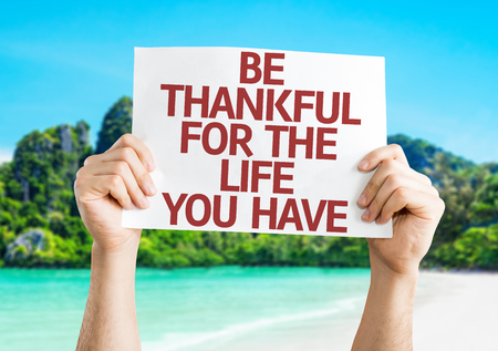 Hands holding Be Thankful for the Life You Have card with island backgroundの写真素材