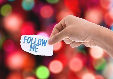 Hands holding Follow Me on a paper with bokeh backgroundの写真素材