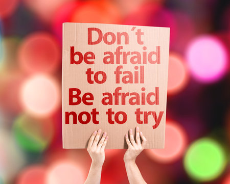 Hands holding cardboard with Don't Be Afraid To Fail Be Afraid Not To Try on bokeh background