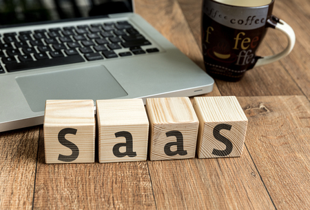 SaaS Software as a service written on a wooden cube in front of a laptopの写真素材