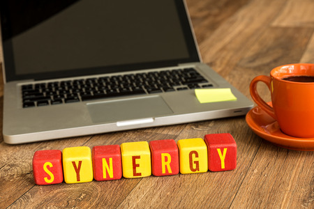 Synergy written on a wooden cube in front of a laptopの写真素材