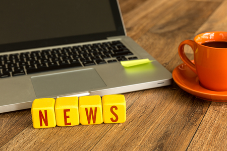 News written on a wooden cube in front of a laptopの写真素材