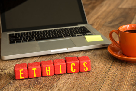 Ethics written on a wooden cube in front of a laptopの写真素材